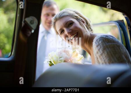 Portrait einer jungen erwachsenen Frau, die an ihrem Hochzeitstag aus einem Auto zu ihrem wartenden reifen Vater kommt. Stockfoto