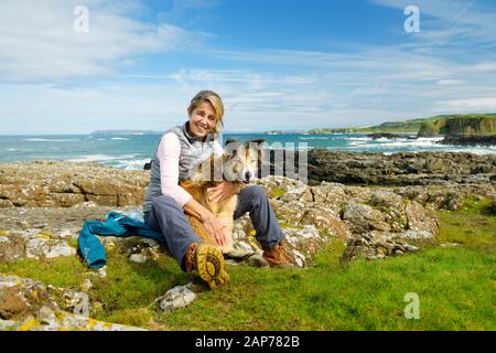 Gesunde Frau im mittleren Alter im Freien im Sommer auf Dem Ulster Way mit Border Collie Dog. Giganten Causeway Küste bei Dunseverick, Co. Antrim, N. Irland Stockfoto