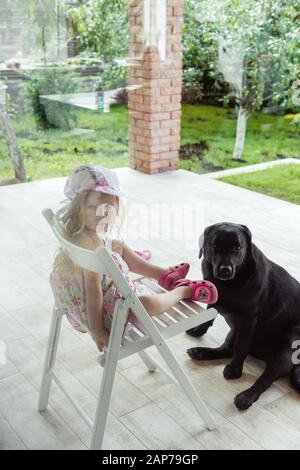 Ein kleines Mädchen sitzt im Hof mit großem labrador Retriever Hund Stockfoto