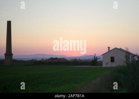 Hoher Turm und weißes Haus mit grünen Feld in Sonnenuntergangsmomenten Stockfoto