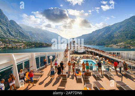 Passagiere an Bord eines oberen Decks einer großen Bootstour auf der Bucht von Kotor oder Boka nähern sich dem adriatischen Hafen von Kotor, Montenegro Stockfoto