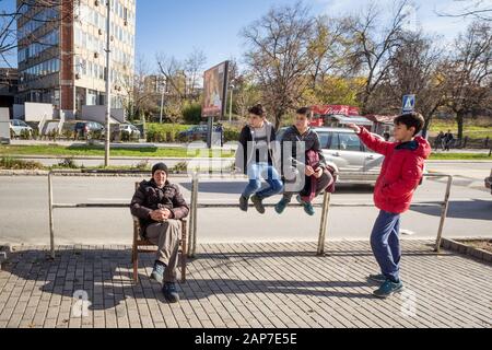 Prishtina, KOSOVO - 13. NOVEMBER 2016: Alter Mann, leitender Rentner, neben einer Gruppe von Jugendlichen, Jugendlichen, im Stadtzentrum von Prishtina sitzend, Stockfoto