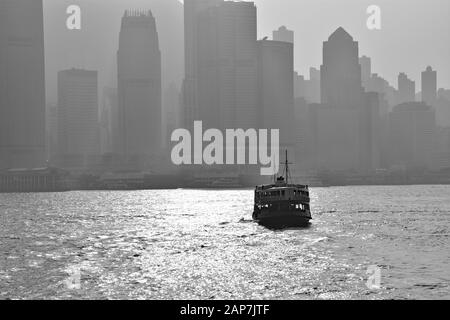 Schwarz-Weiß-Bild der Kreuzung der Star Ferry zwischen Central District und Kowloon Peninsula mit einem Smog, der über der Innenstadt von Hongkong hängt. Stockfoto