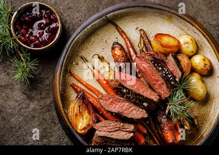 Gegrilltes Wildsteak mit gebackenem Gemüse und Beerensauce auf dunklem Hintergrund Stockfoto