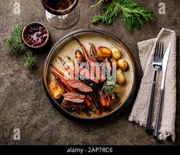 Gegrilltes Wildsteak mit gebackenem Gemüse und Beerensauce und Rotwein auf dunklem Hintergrund Stockfoto