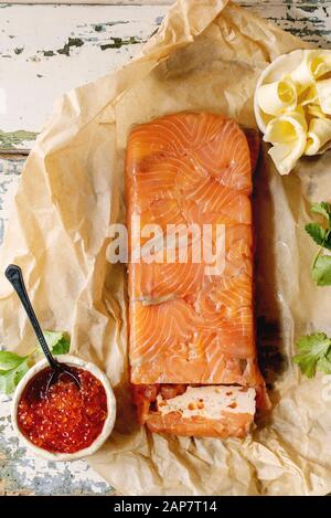 Roter Lachskaviar in Keramik Schüssel und Hausgemachte Terrine von Lachs serviert mit Butter auf zerknittertes Papier über alten Holztisch. Flach, Raum Stockfoto