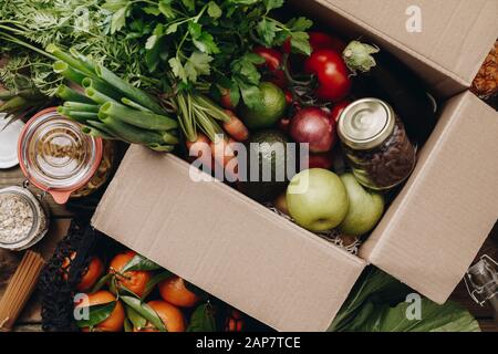 Lebensmittelauswahl in Papierbox: Obst, Gemüse, Kräuter, Hülsenfrüchte, Getreide, Blattgemüse auf Holzgrund. Gesundes Essen, sauberes Essen, Diäten, Kochen Stockfoto