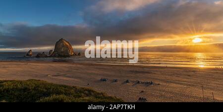 Blick auf den Sonnenuntergang am Cannon Beach mit Haystack Rock und Sonnenstrahlen. Stockfoto
