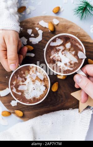 Frau und Mann, die eine Tasse veganer Mandelmilch heiße Schokolade mit Kokosbutter, Kokosnuss und Mandeln halten. Stockfoto