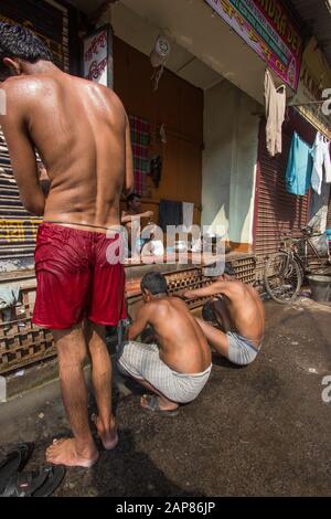 Männer und Jungen sind mit dem Baden und Reinigen auf der Straße beschäftigt. Wasserleitungen sind für Waschbedarf eingeschaltet. In Kalkutta (Kalkutta), Indien. Stockfoto