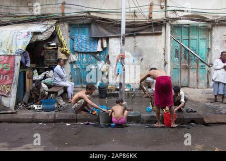 Männer und Jungen sind mit dem Baden und Reinigen auf der Straße beschäftigt. Wasserleitungen sind für Waschbedarf eingeschaltet. In Kalkutta (Kalkutta), Indien. Stockfoto