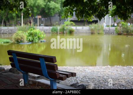 Schattige Parkbank neben einem ruhigen Teich in der Stadt Neu-Taipeh Stockfoto