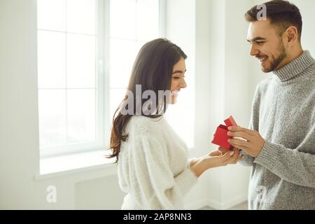 Der Kerl macht dem Mädchen einen Heiratsantrag. Lächelnder Mann gibt einen Ring des Heiratsanschlags im Zimmer. Stockfoto