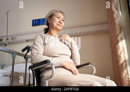 Traurige und depressive asiatische Seniorin, die allein im Rollstuhl im Pflegeheim sitzt Stockfoto