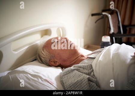 Kranker asiatischer Mann, der im Krankenbett liegt, scheint traurig und hilflos zu sein Stockfoto