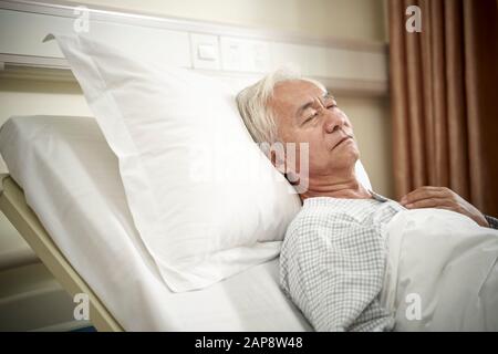 Älterer asiatischer männlicher Patient liegt im Bett und schläft in der Krankenstation oder in der betreuten Wohneinrichtung Stockfoto