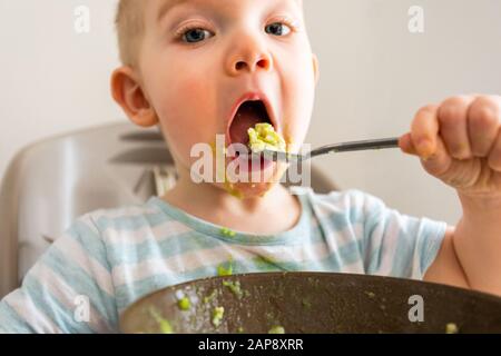 Kleiner Junge allein isst Püree aus einer Platte. Stockfoto