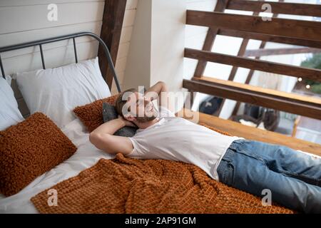 Lächelnder junger Mann, der sich in seinem Schlafzimmer entspannen konnte Stockfoto