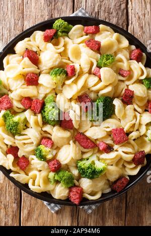 Italienische Nudelorecchiette mit Brokkoli und Würstchen in cremiger Sauce in einem Teller auf dem Tisch. Vertikale Draufsicht von oben Stockfoto