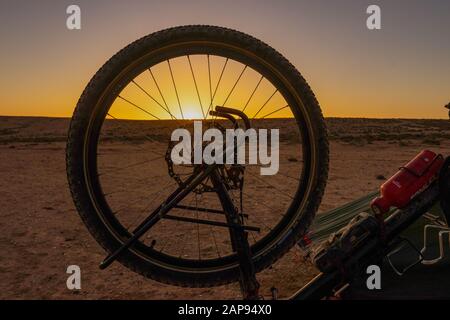Sonnenaufgang in der Wüste im Süden von marokko, vorne das Rad eines Wanderrades Stockfoto