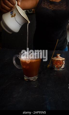 Hand der Frau, die Milch in Kaffee gießt, mit Zuckerdose im Hintergrund. Loft-Stil Instagram gießen Schuss. Mandelmilch in veganen Kaffee gegossen, rübergießen Stockfoto