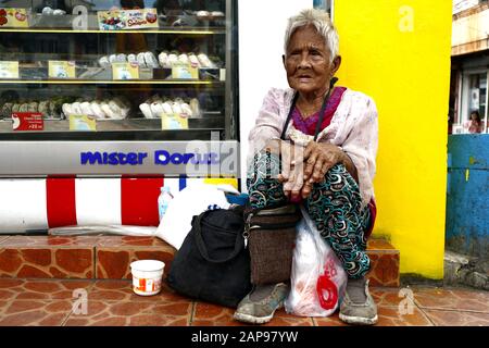 Antipolo City, Philippinen - 18. Januar 2020: Die alte philippinische Frau sitzt auf einem Bürgersteig und bittet die Menschen, ihr Essen oder Almosen zu geben. Stockfoto