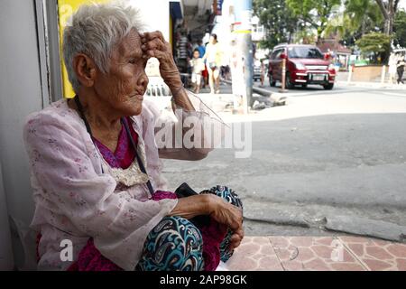 Antipolo City, Philippinen - 18. Januar 2020: Die alte philippinische Frau sitzt auf einem Bürgersteig und bittet die Menschen, ihr Essen oder Almosen zu geben. Stockfoto