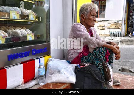 Antipolo City, Philippinen - 18. Januar 2020: Die alte philippinische Frau sitzt auf einem Bürgersteig und bittet die Menschen, ihr Essen oder Almosen zu geben. Stockfoto