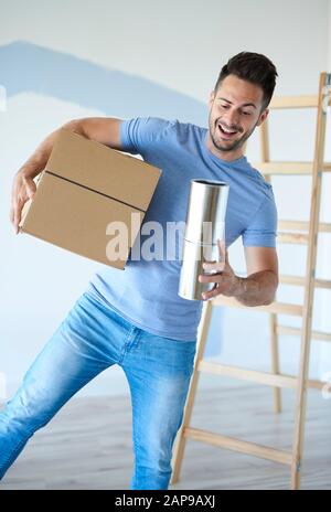 Der junge Mann, der Kasten und Farbe hält, kann in seiner neuen Wohnung Stockfoto