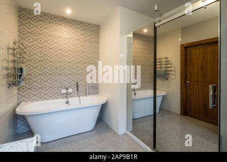 Blick auf die weiße Badewanne mit Dusche im Bad. Spiegel an der Wand. Geschlossene Holztür. Stockfoto