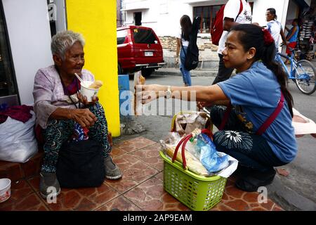 Antipolo City, Philippinen - 18. Januar 2020: Die alte philippinische Frau sitzt auf einem Bürgersteig und bittet die Menschen, ihr Essen oder Almosen zu geben. Stockfoto