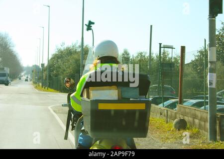 Postbote bei der Arbeit an ihrem Roller in der Kälte, die ihre Arbeit bei der Zustellung von Post an Bürger für den öffentlichen Dienst auf den Straßen einer Stadt mitten in t erledigt Stockfoto