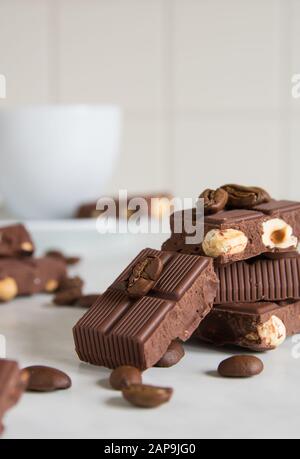 Stücke Schokolade mit Haselnüssen und Kaffeebohnen auf einem Marmortisch Stockfoto