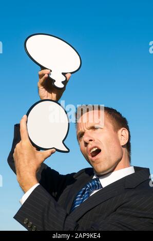 Verwirrter Geschäftsmann, der gemischte Botschaften mit leeren Sprechblasen und Gedankenblasen ausgab Stockfoto