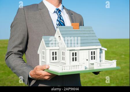 Immobilienmakler hält Modell auf einem hellgrünen Rollfeld zu Hause Stockfoto
