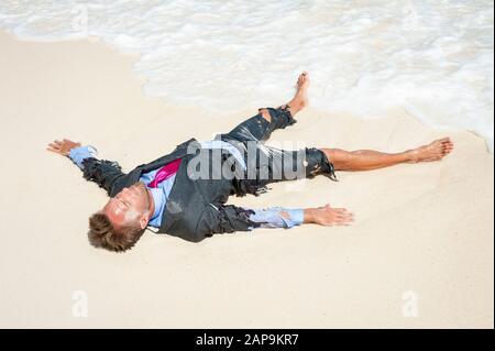 Castaway survivor Geschäftsmann an einem tropischen Strand in ein zackiges zerrissen Anzug Stockfoto