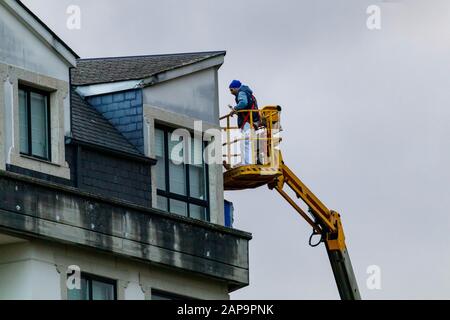 Coruna/Spanien - 22. Januar 2020: Mann, der mit einem selbstfahrenden Cherry Picker an der Reparatur eines Wohnblocks arbeitet Stockfoto