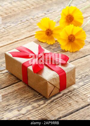 Geschenkbox mit rotem Band und gelben Blumen auf alten Holzbrettern. Draufsicht. Stockfoto
