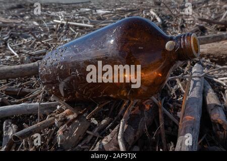 Schmutziger Strand nach dem Sturm, Flasche und Holzstämme auf dem Sand Stockfoto