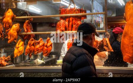 Selektive Konzentration auf einen Mann mit Hut, der geröstetes Huhn und Enten durch ein Restaurantfenster in Chinatown sieht. Stockfoto