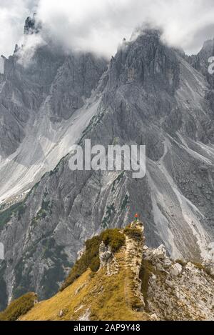 Bergsteigerin, Frau, die auf einem Grat steht und in eine zirke, dramatische Wolke blickt, in den hinteren Felswänden von Cimon di Croda Liscia, Auronzo di Stockfoto