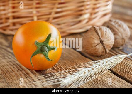 Gelbe Tomate, Walnüsse, Weizenähren und Korbkorb auf Holzgrund aus der Nähe. Geringe Schärfentiefe. Stockfoto