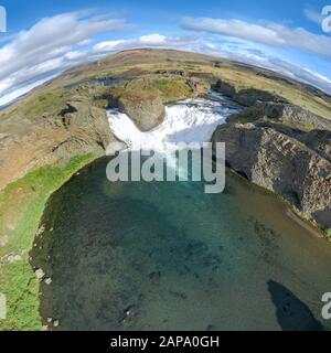 Epischer Luftdronblick, der an einem sonnigen Tag über die Landschaft des Hjalparfoss Wasserfalls und der Lagune fliegt. Stockfoto