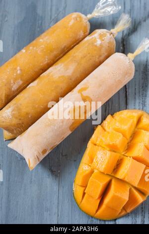 Drei Mango chia Lollies auf blauem Grund mit einem Mango-Schnitt in der Hälfte Stockfoto