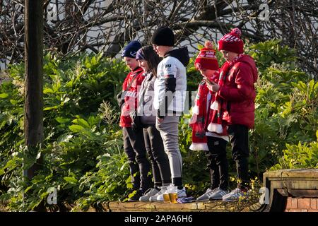 Kleine Kinder, die LFC-Farben tragen, stehen an einer Wand und warten darauf, den anreisenden Teamtrainer des FC Liverpool bei Anfield Liverpool zu begrüßen. Stockfoto
