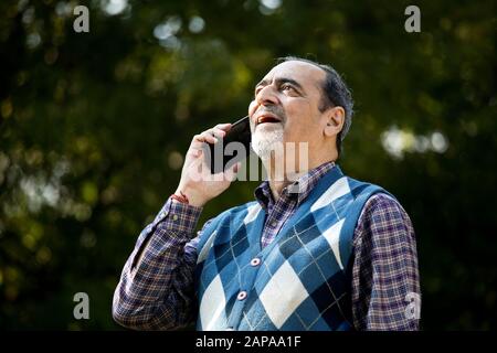Glücklicher älterer Mann, der das Telefon im Park benutzt Stockfoto