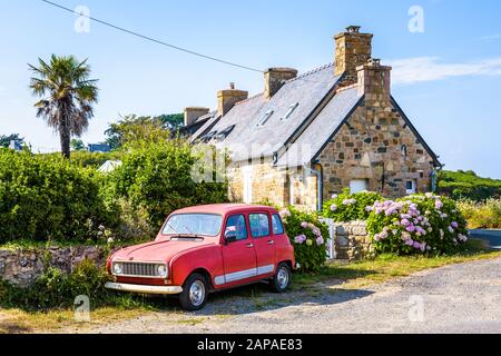 Ein französisches Oldtimer, das vor einem typischen bretonischen Granithaus mit Schieferdach, Palmen und Hortensien bei einem sonnigen Tag in der Bretagne, Frankreich, geparkt wurde. Stockfoto