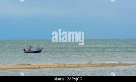 Traditionelles thailändisches Segelboot hinter Sandbar mit Vögeln am Strand in Pak Nam Pram, Thailand Stockfoto