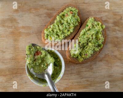 Draufsicht auf kleine Tasse und Löffel mit Guacamole neben Sandwiches, die auf einem Holztisch liegen Stockfoto