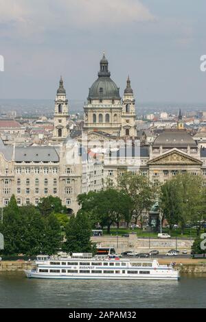 Budapester Kreuzfahrtschiff auf der Donau mit der Stephanusbasilika und der Stadt Budapest im Hintergrund hinter der Donau an einem sonnigen Frühlingstag. Stockfoto